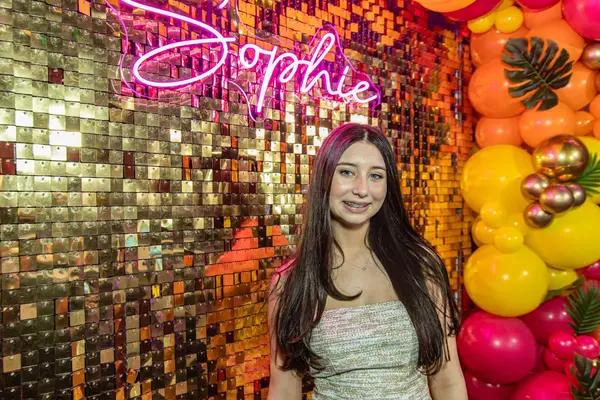 The honoree at the gold sequin wall with Sophie neon sign