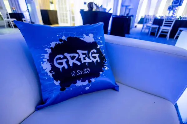 Blue satin Greg logo pillow on a white lounge sofa