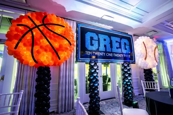 Lit GREG sign between giant balloon basketball and baseball sculptures