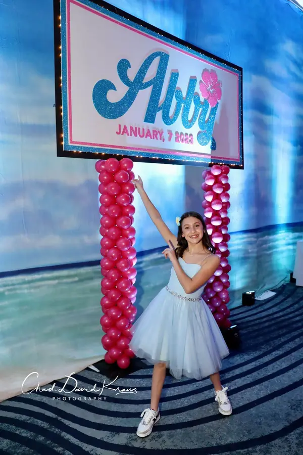 The honoree under the Abby logo sign with pink balloon columns