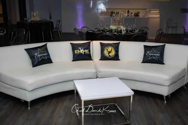 White curved lounge with Emme logo pillows and acrylic table