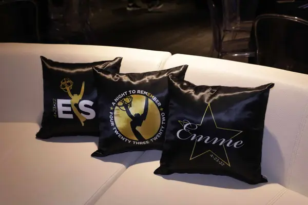 Three black satin Emme logo pillows on a white lounge sofa