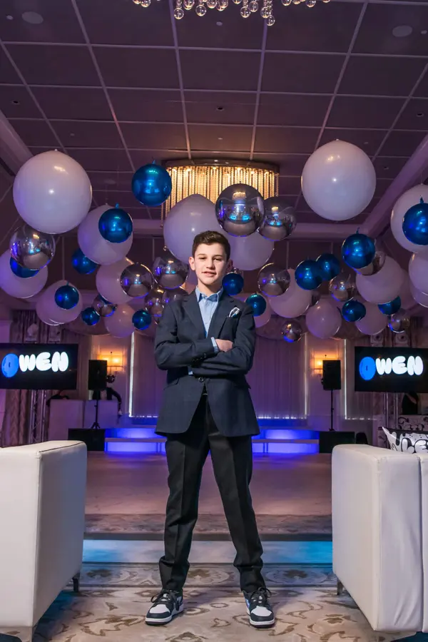 Owen's Bar Mitzvah honoree beneath white and blue ceiling balloons