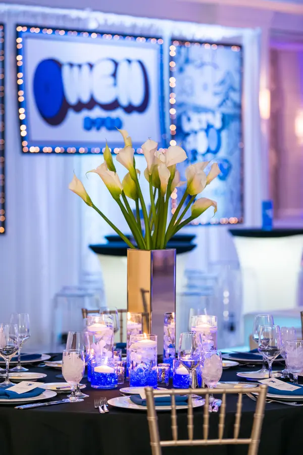 Owen's Bar Mitzvah calla lily centerpiece in front of the logo backdrop